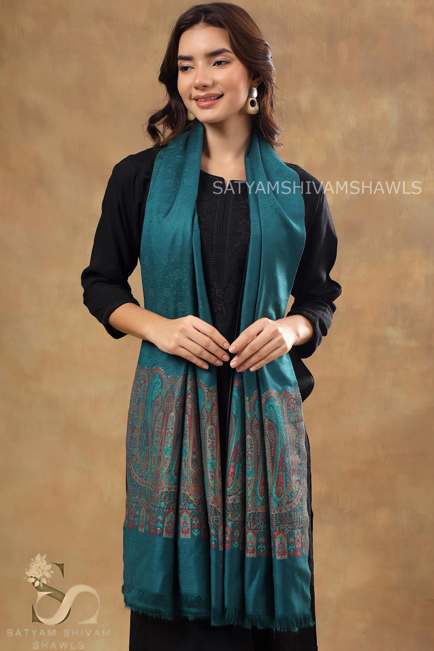 Woman wearing a teal shawl with intricate patterns on a brown background, featuring the brand 'Satyam Shivam Shawls'.