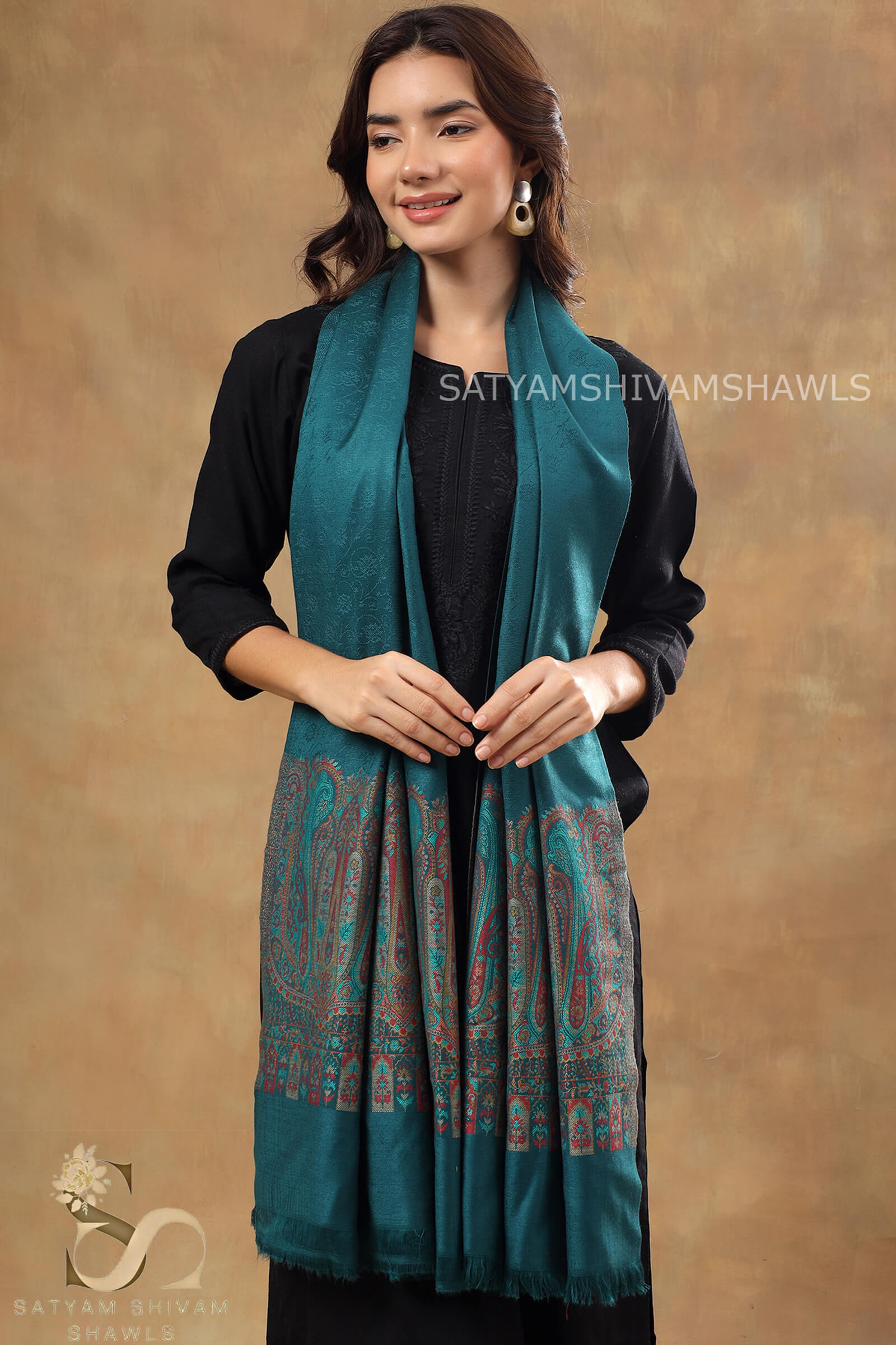 Woman wearing a teal shawl with intricate patterns on a brown background, featuring the brand 'Satyam Shivam Shawls'.